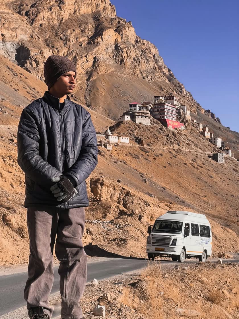 Raj, founder of Lets Chale, standing by a mountain road in Spiti Valley with a hillside monastery behind him